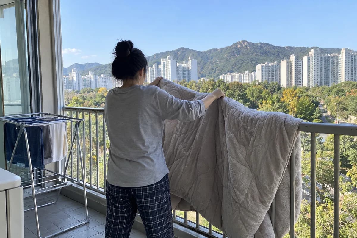 가을 개운법 대표 이미지, 초가을 아침 베란다 난간에 이불을 널고 터는 사람 airing out
